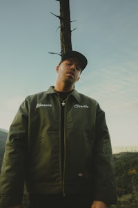 a man in a green jacket standing next to a tree