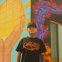 a man wearing a black t - shirt standing in front of a colorful wall