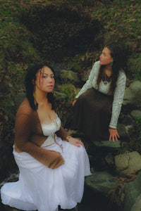 two women sitting on a rock next to a stream